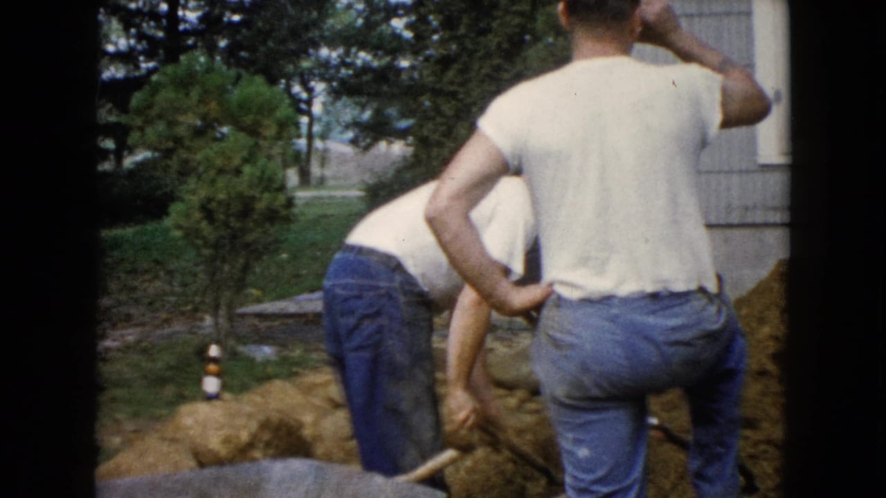 One man bends over the dirt while another stands with a hand on his hip.