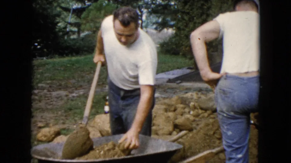 1960 Wauconda backyard construction frame with a man shoveling soil and another adult man seen from behind.
