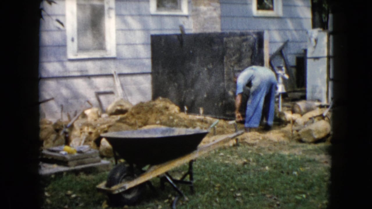 In Wauconda, Illinois, a man in blue overalls works beside a house during a 1960 backyard landscaping project.