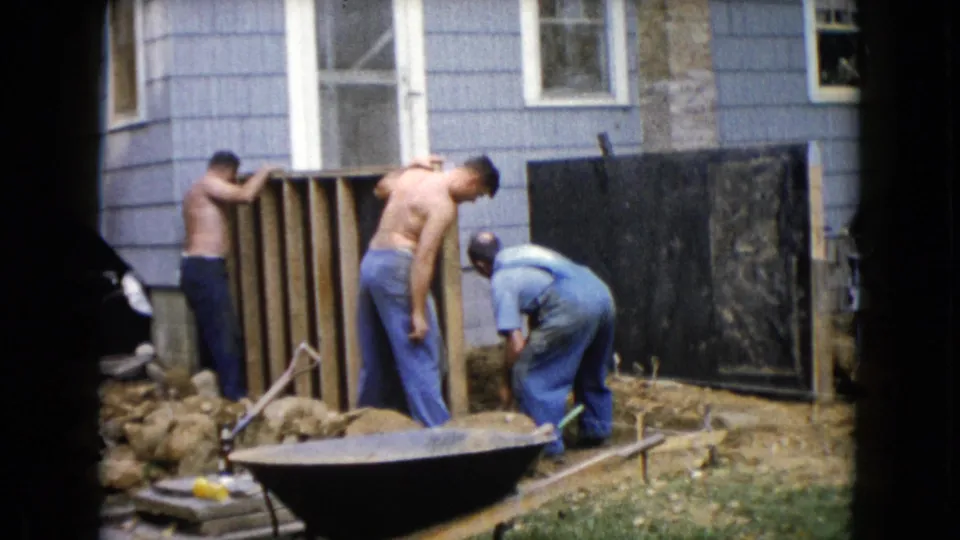 A 1960 Wauconda backyard scene shows men handling a small construction area near house siding, rocks, and tools.