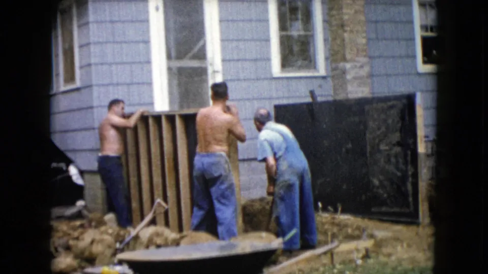 At the end of the short 1960 Wauconda clip, three men pause or reposition near a backyard wooden structure beside the house.