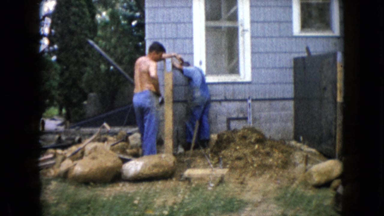 In Wauconda, Illinois in 1960, three adult men work on a backyard construction project beside a gray-sided house.