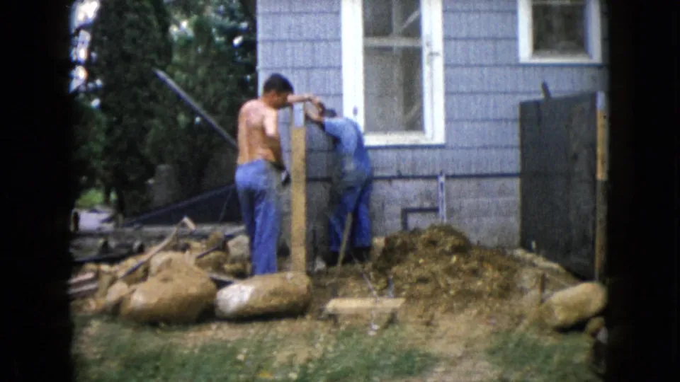 In Wauconda, Illinois in 1960, three adult men work on a backyard construction project beside a gray-sided house.