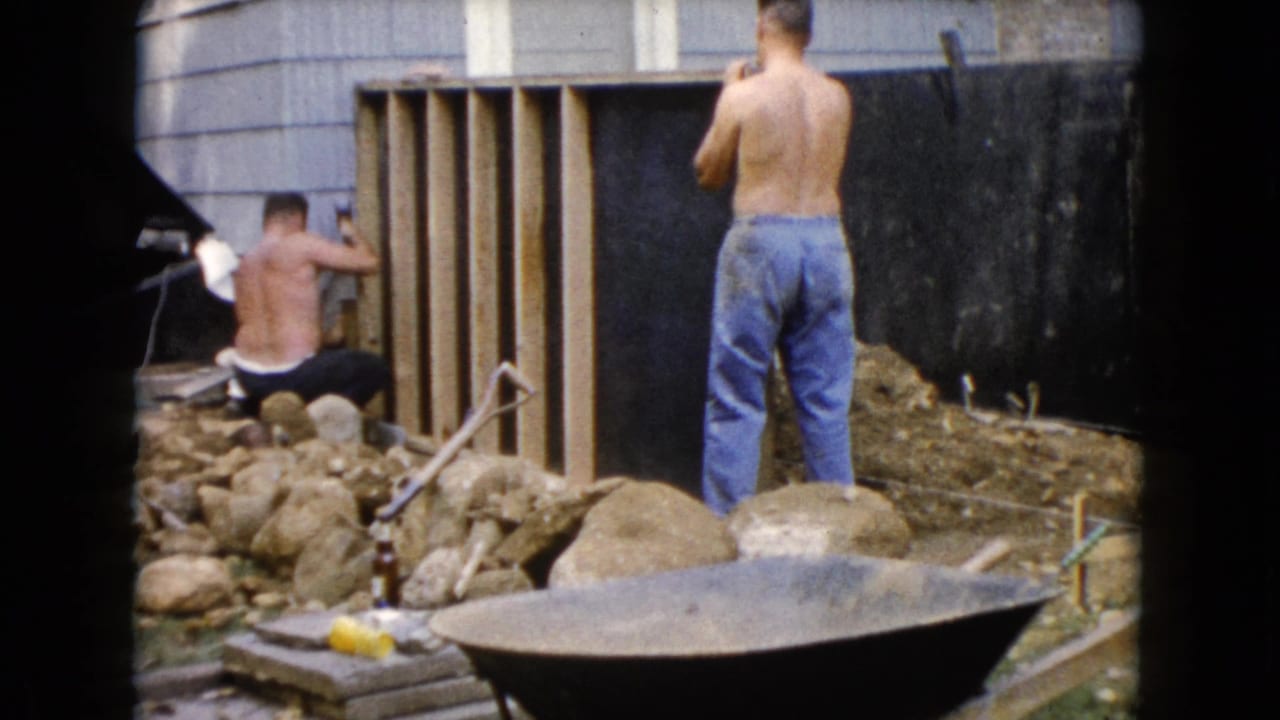 In Wauconda, Illinois, 1960 home-movie footage shows shirtless men working near a wooden frame, rocks, tools, and a wheelbarrow.