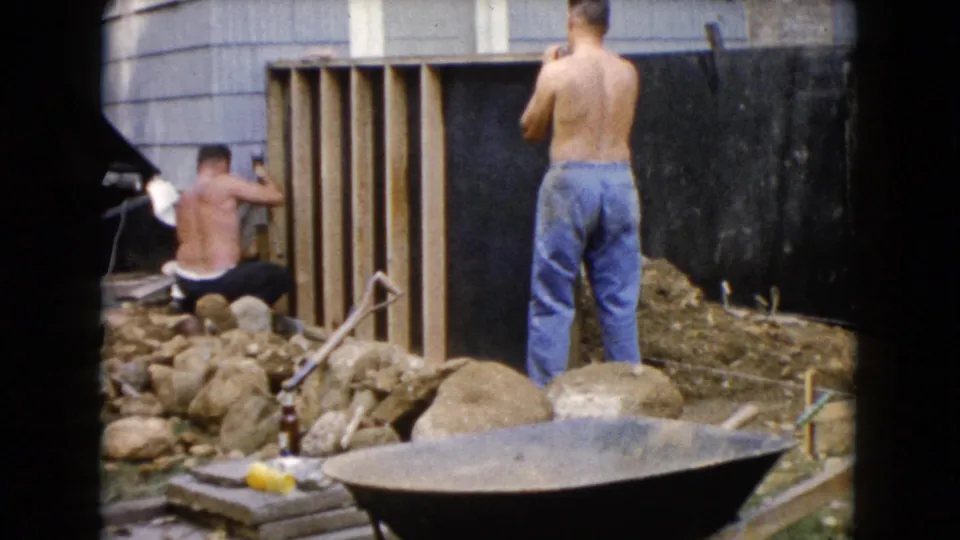 In Wauconda, Illinois, 1960 home-movie footage shows shirtless men working near a wooden frame, rocks, tools, and a wheelbarrow.