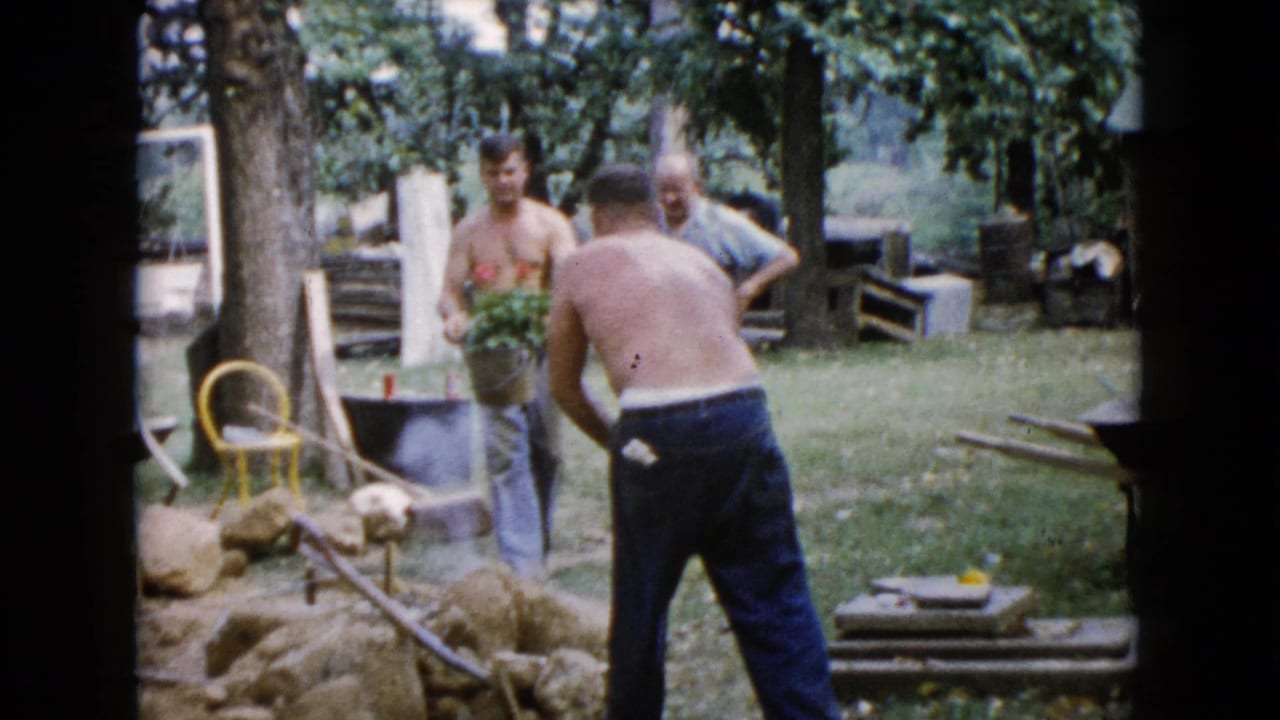 1960 Wauconda backyard scene with men handling a shovel and a bucket of plants near rocks and scattered garden materials.