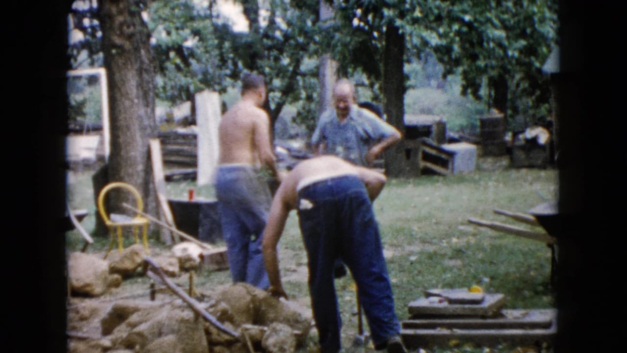 1960 Wauconda backyard frame with two shirtless men working near rocks while an older man in a blue shirt observes.