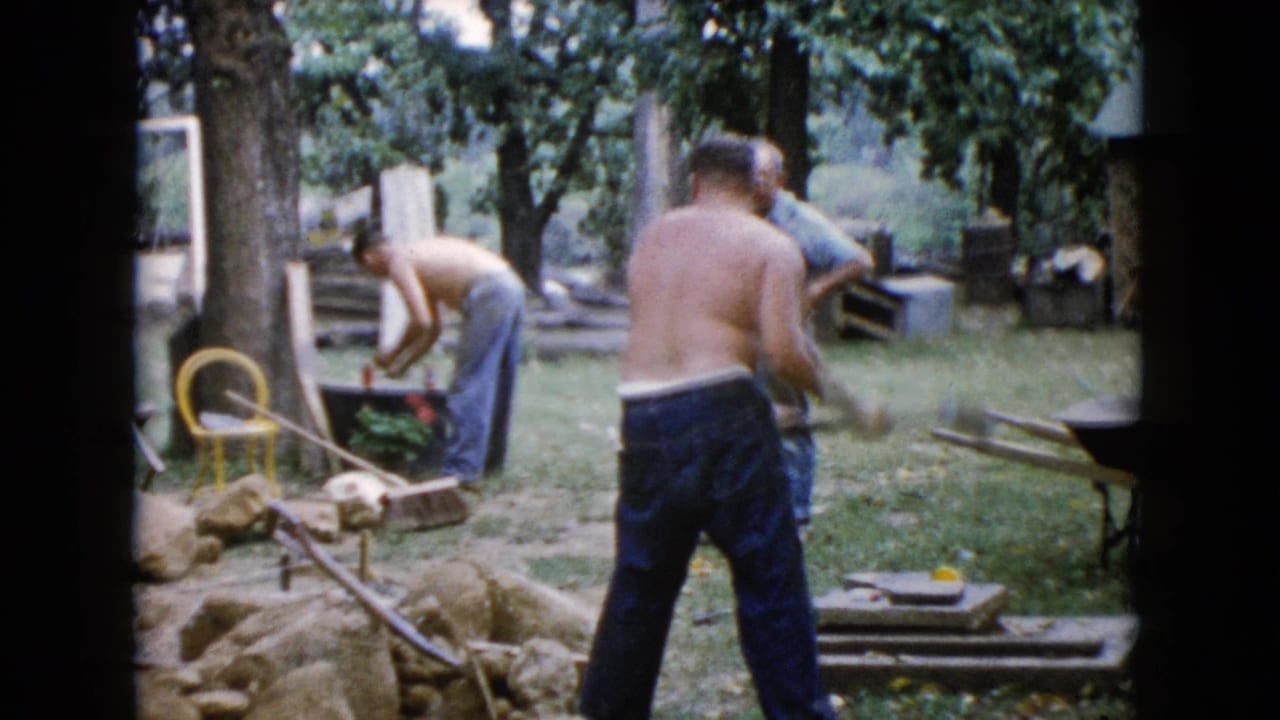 Men working around rocks and tools in a grassy backyard.