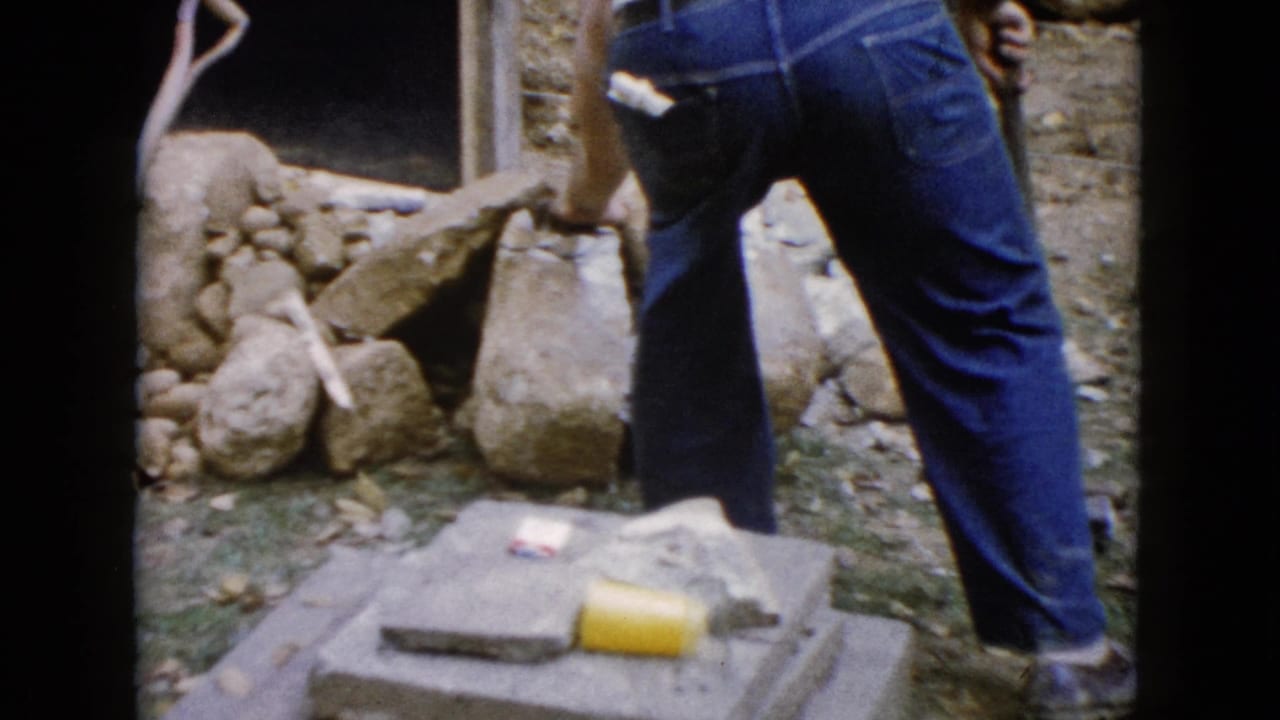 A man in jeans stands at a rough outdoor stone work area in the 1960 Wauconda, Illinois home-movie footage.