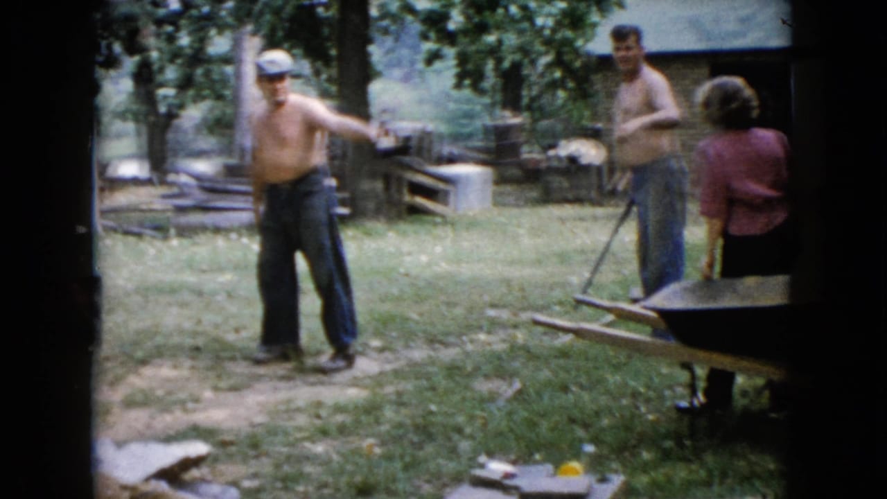 In a 1960 Wauconda, Illinois backyard scene, a shirtless man gestures with a sledgehammer while two adults stand nearby.