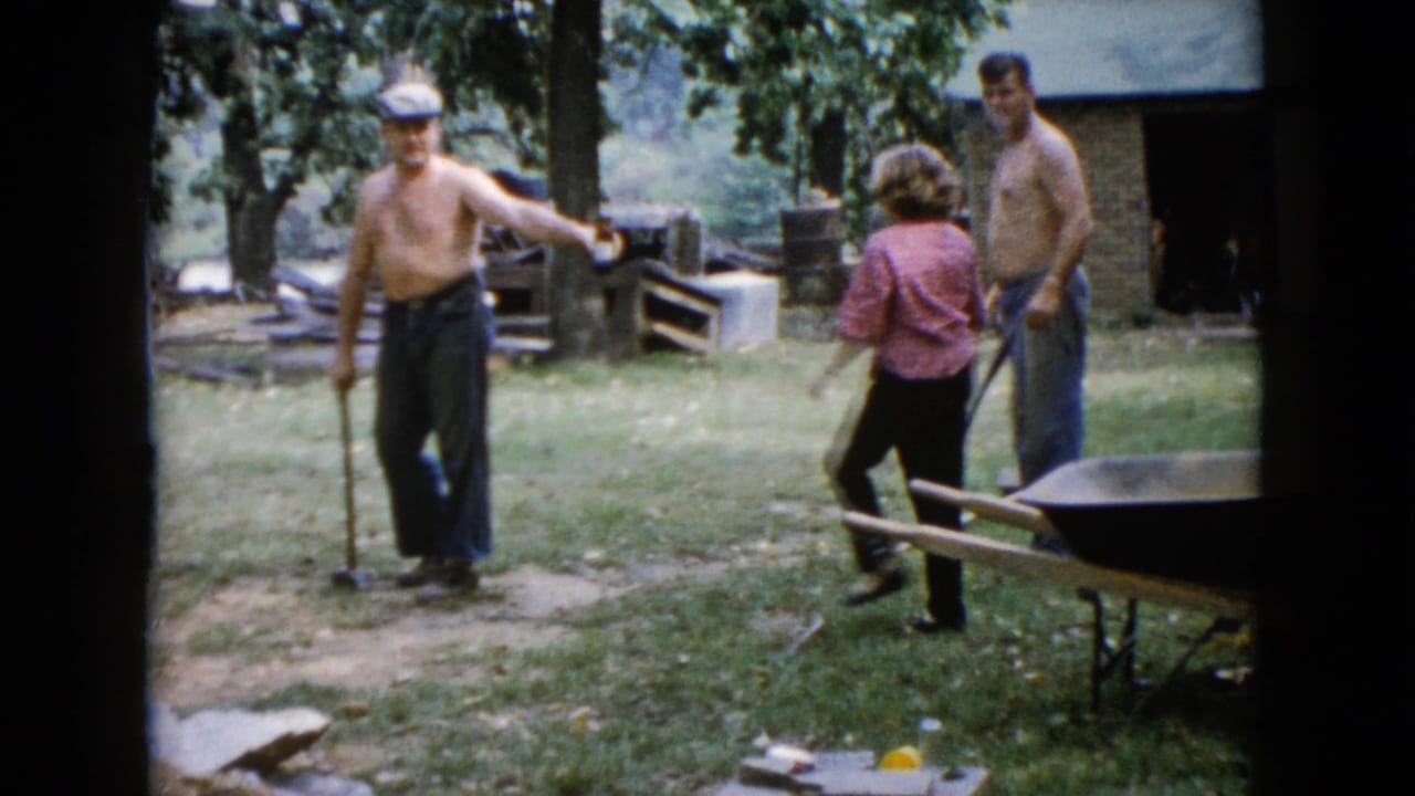 The backyard work scene continues as the man with the sledgehammer stands near a path while two adults reposition nearby.