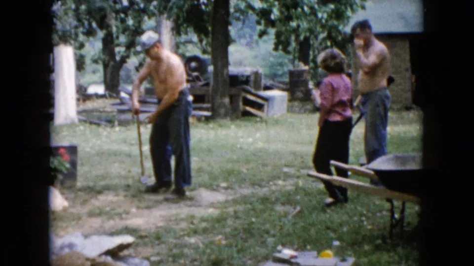 In the Wauconda yard, the shirtless man brings the sledgehammer down near a post or work spot as the others watch close by.