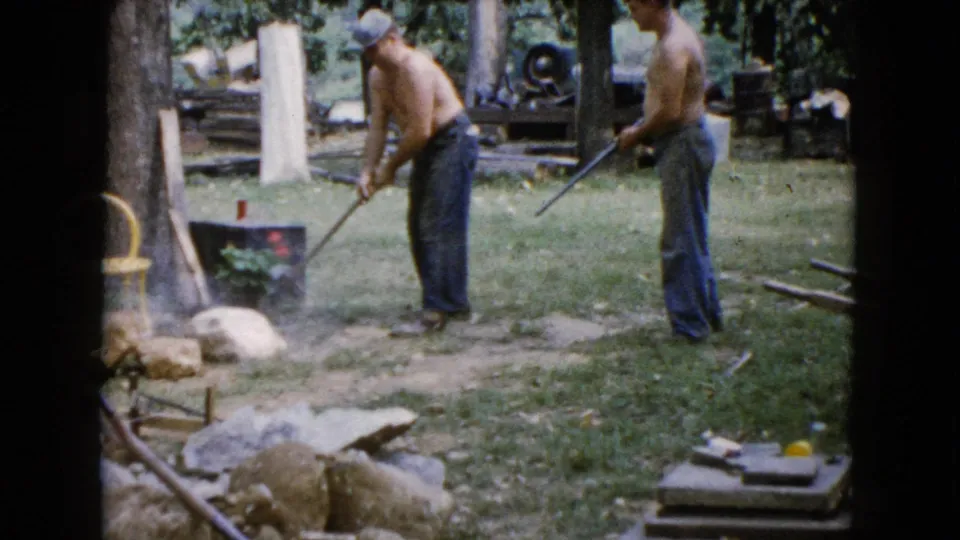 The 1960 home-movie frame shows two men with tools after a hammer strike in a grassy yard in Wauconda, Illinois.