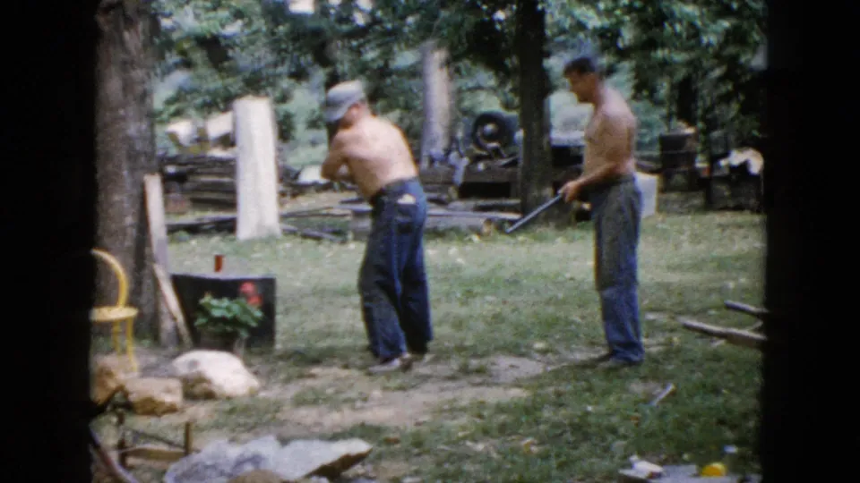 The final frame shows the shirtless hammering man turned beside the rock, with another man holding a long-handled tool in the Wauconda yard.