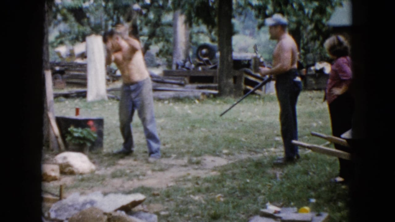 In 1960 Wauconda, Illinois home-movie footage, a shirtless man swings a sledgehammer in a grassy yard as two adults watch.