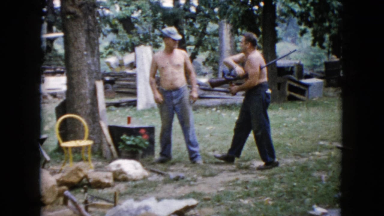 In the 1960 Wauconda backyard scene, one shirtless man gestures upward with a long gun as another stands nearby.