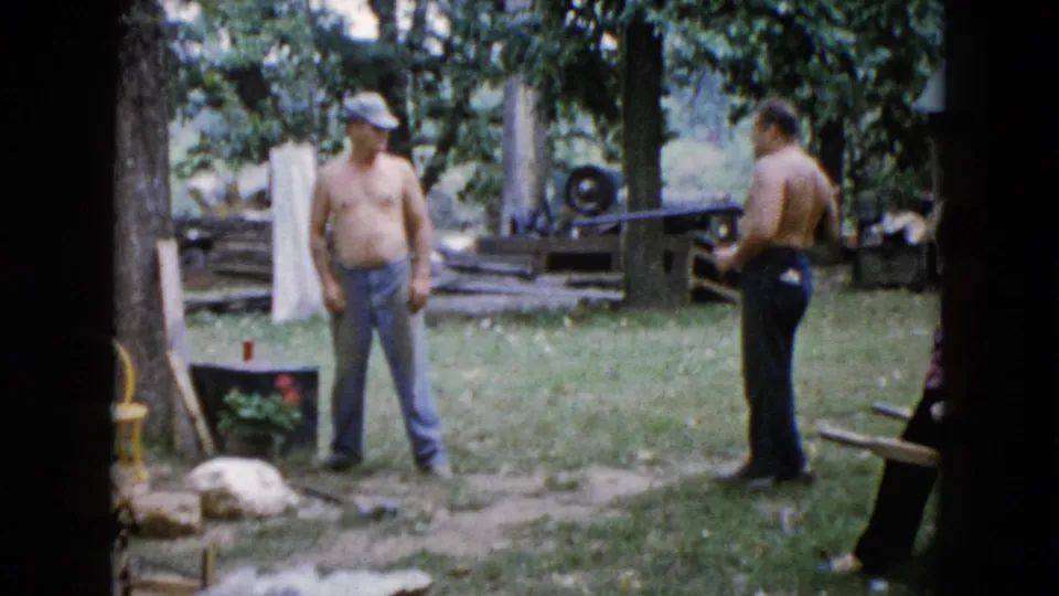 In Wauconda, Illinois home-movie footage from 1960, two shirtless men stand in a yard as one holds a rifle-like long gun.