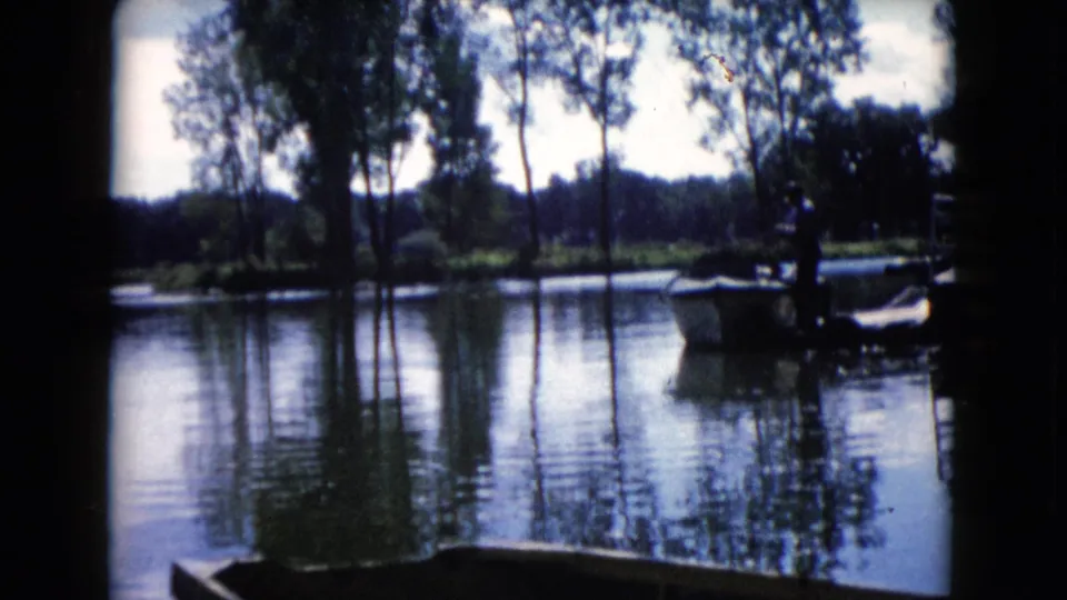 1960 Wauconda, Illinois frame with the small boat partly at right, calm water, tree reflections, and visible 8mm frame edges.