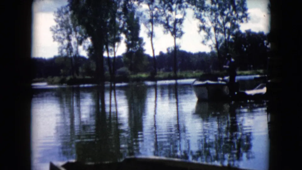 1960 8mm home-movie frame from Wauconda, Illinois, showing a man by a small boat on a tree-lined lake.