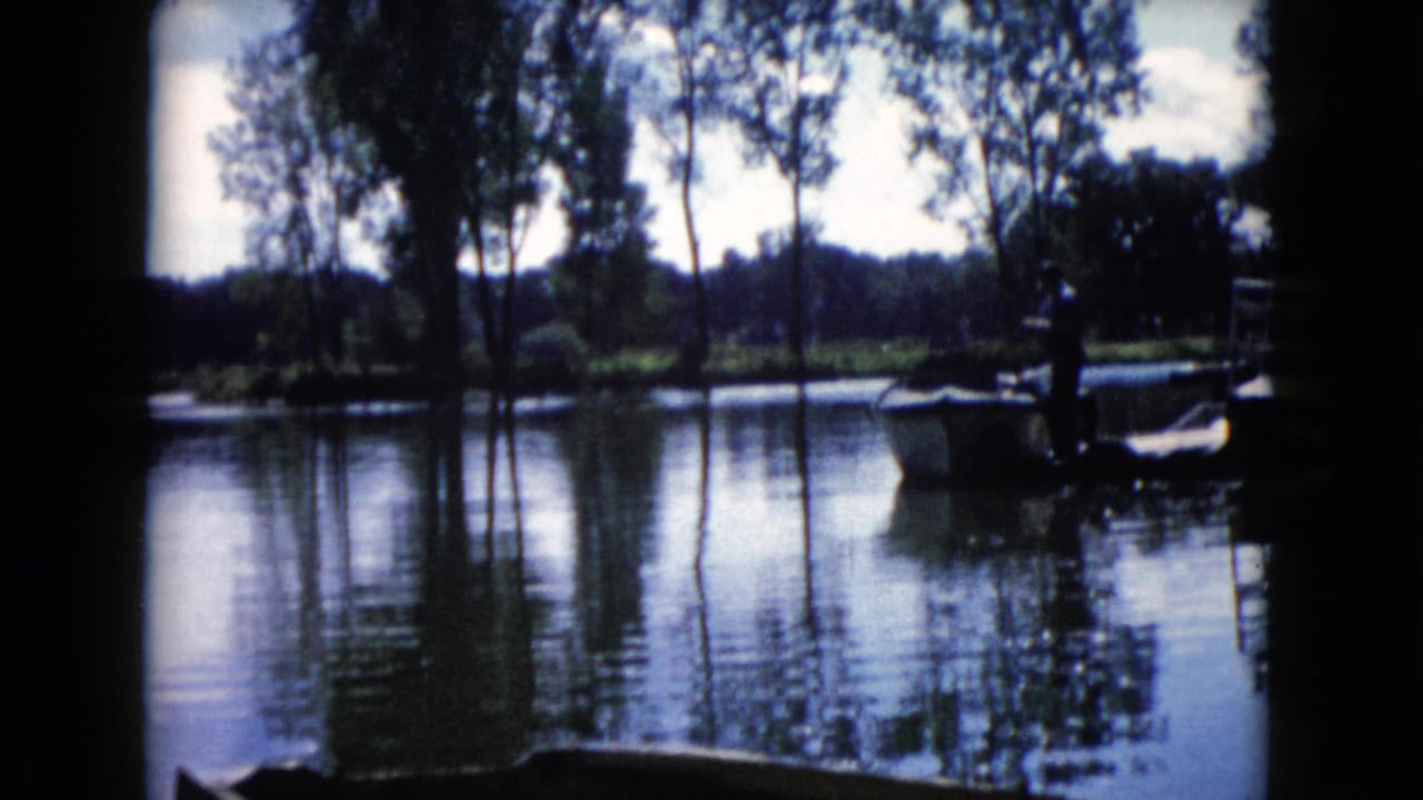 Wauconda, Illinois lake scene on 8mm film, with a man silhouetted beside a small boat and rippled reflections.