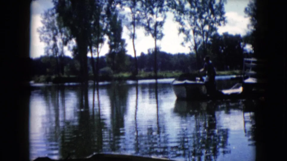 End frame of the 1960 Wauconda lake clip, showing a silhouetted man near a small boat under tall trees.