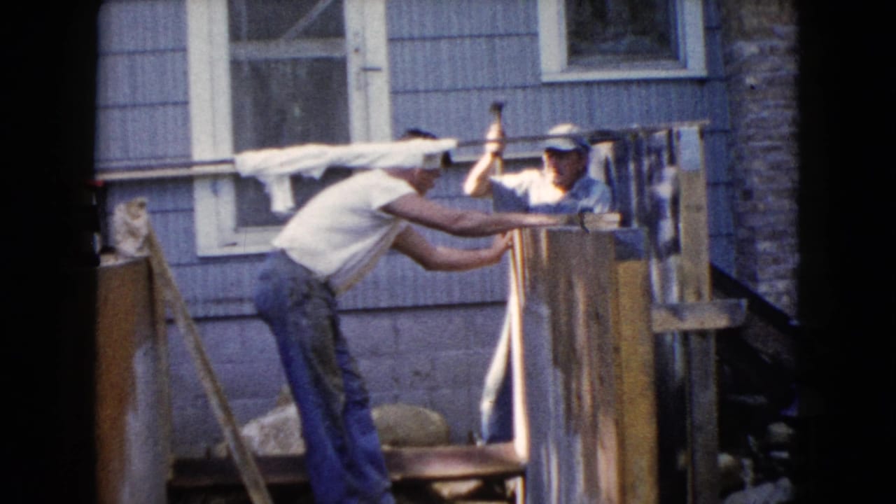 One man prepares to strike with a hammer while another holds the wood in place outside the Wauconda house.