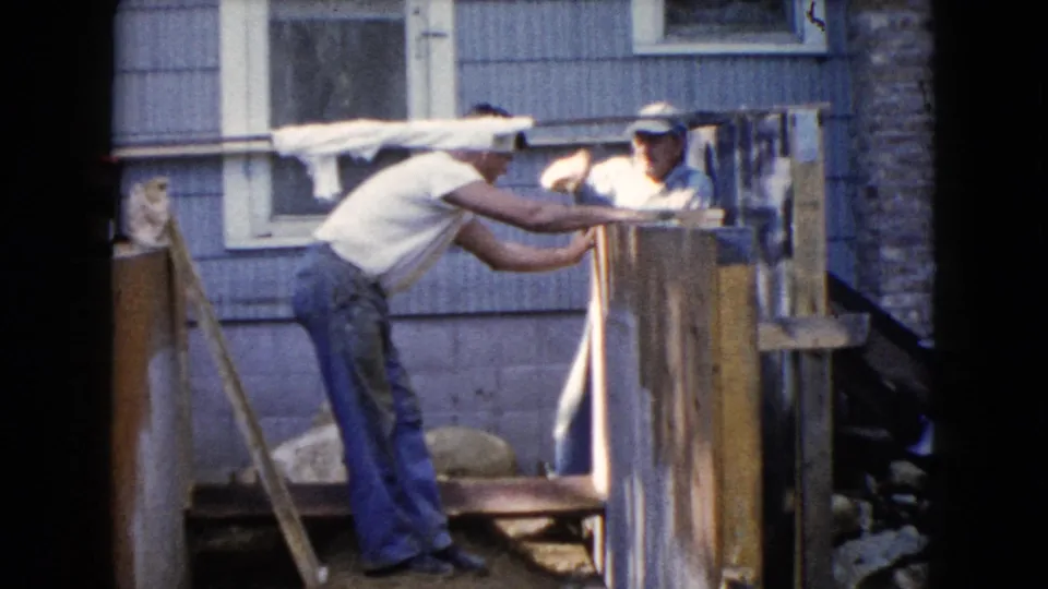 At the end of the clip, two men remain at the wooden structure, one hammering while the other steadies the work.