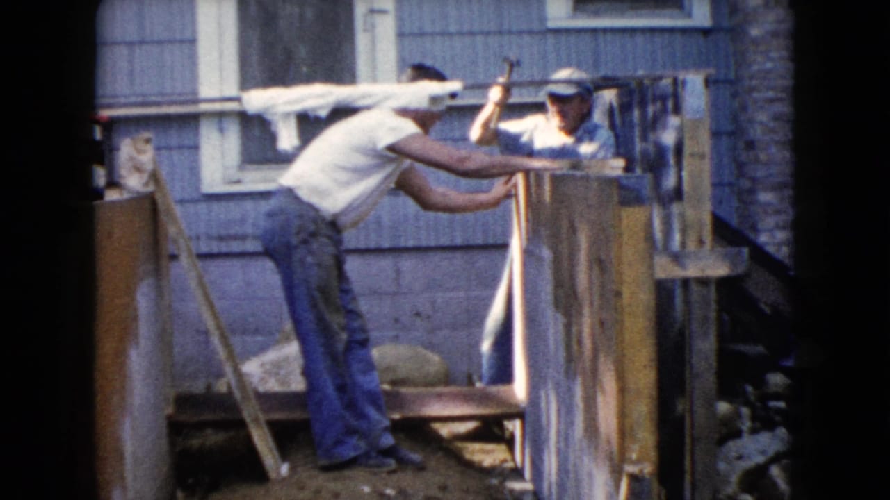 A backyard work scene shows one man leaning over boards as another man in a cap prepares to hammer the wooden frame.