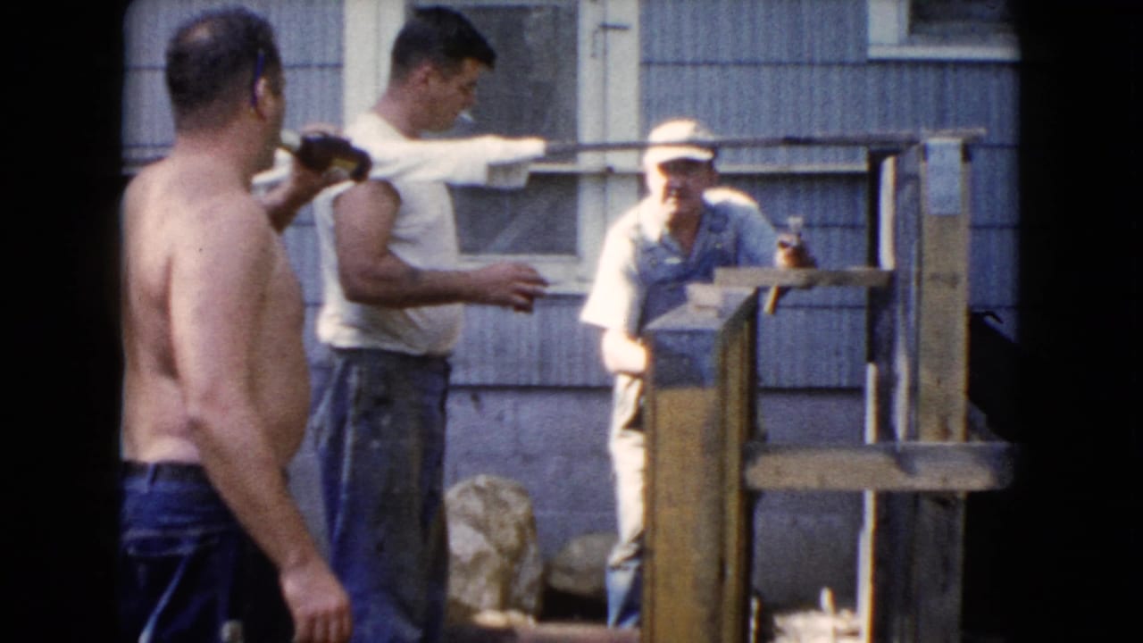 In Wauconda, Illinois home-movie footage from 1960, three adult men gather outside a house beside a partly built wooden structure.