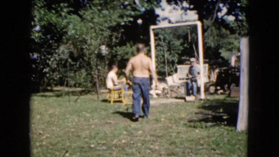 A wider 1960 Wauconda backyard view shows adults spread around a lawn with chairs, trees, and a simple swing set frame.