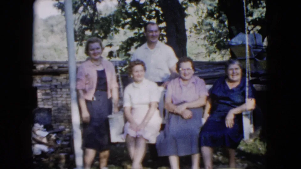The group faces the camera in a 1960 Wauconda garden portrait, framed by trees, lawn, a swing set, and a low wall.