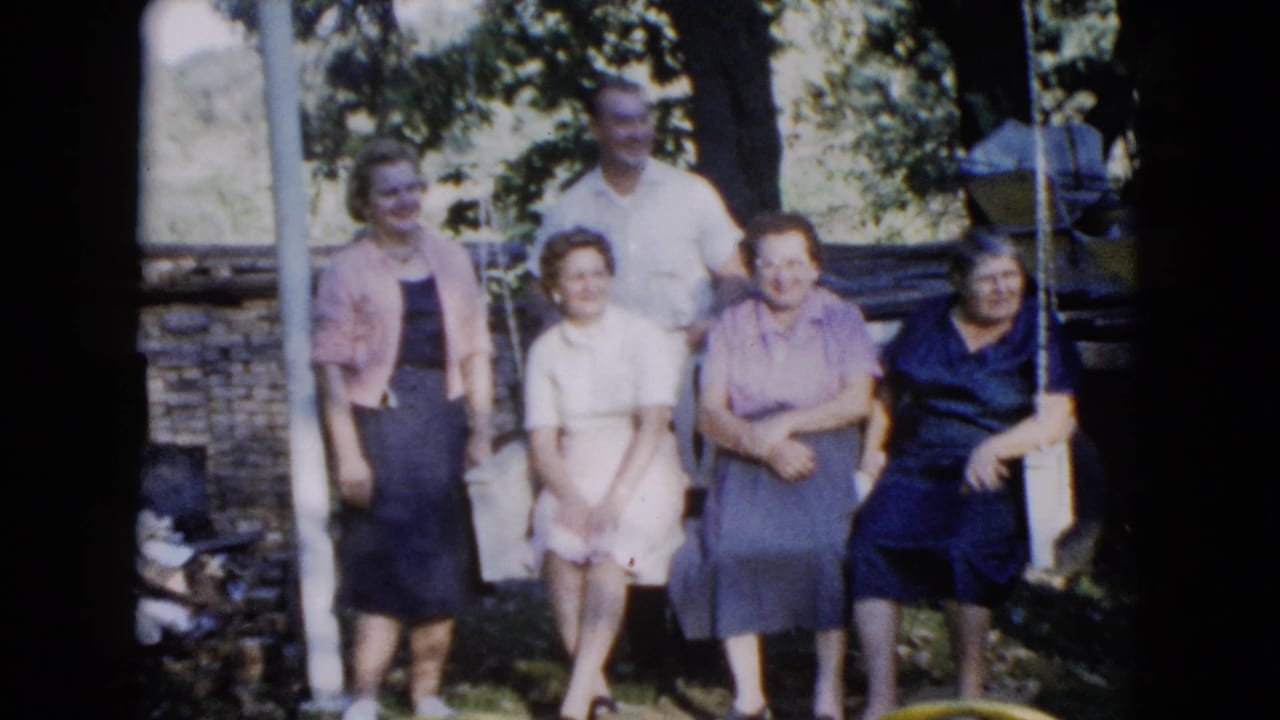 Adults pose outdoors beside and on a yard swing under leafy trees.