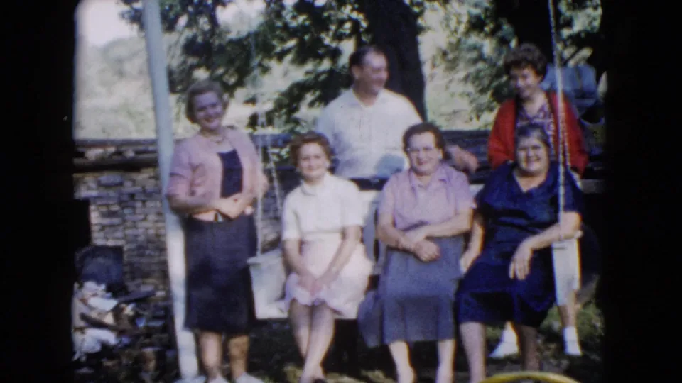 In the 1960 Wauconda home movie, six adults hold a relaxed pose around the yard swing as the camera records slight movement.