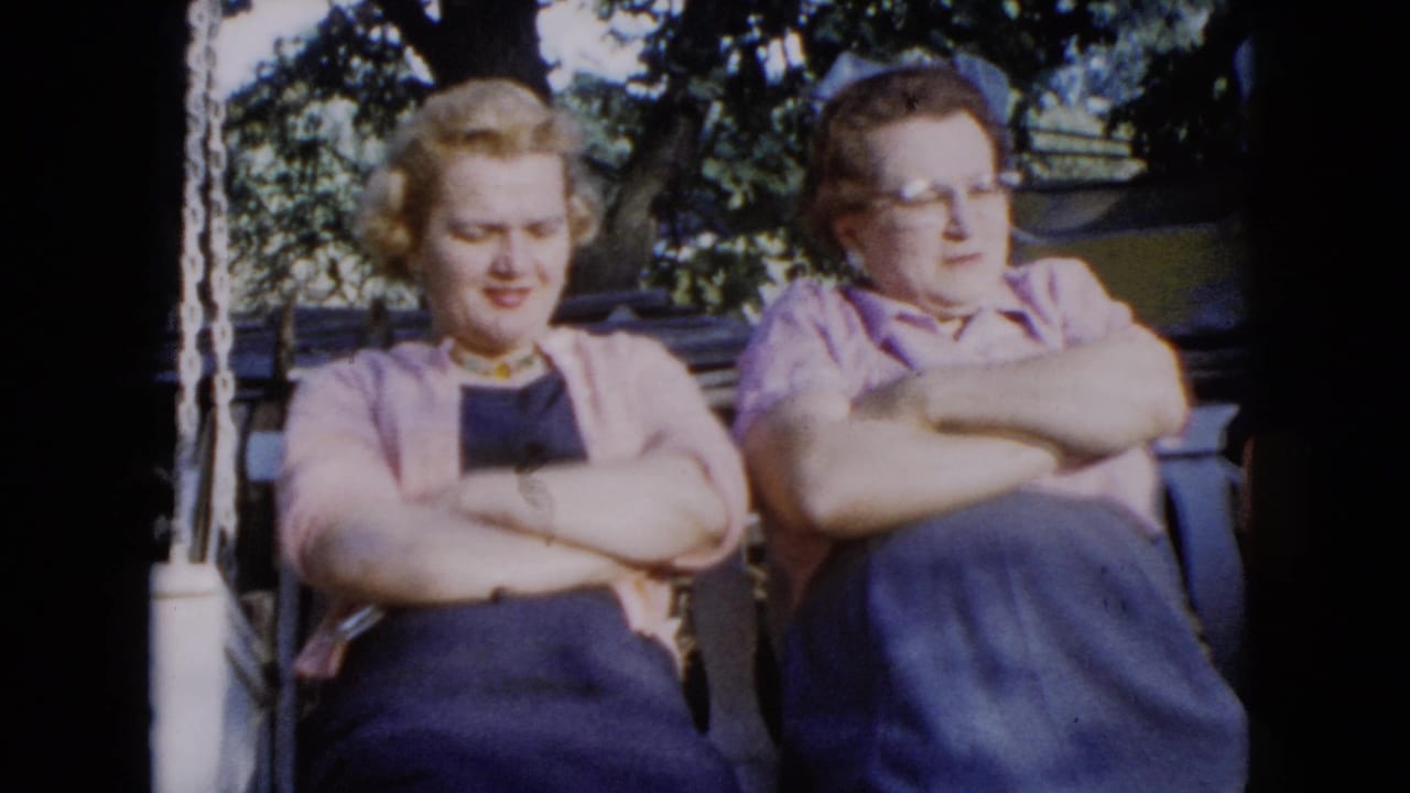 1960 Wauconda home-movie frame showing two women seated outdoors on a porch swing in sun and shade.