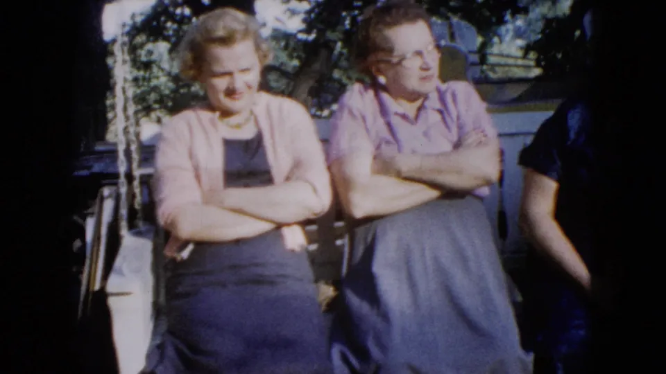 1960 Wauconda frame with two women seated on a shaded porch swing and another person partly cropped at right.