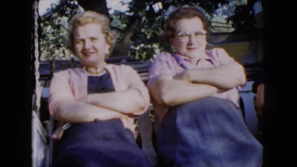 1960 Wauconda home-movie frame of two women seated close together on a porch swing, facing the camera.