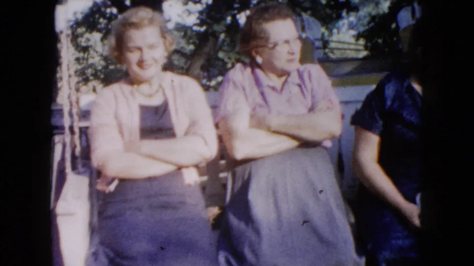 1960 Wauconda frame showing two women on a porch swing and a cropped third person at the right edge.