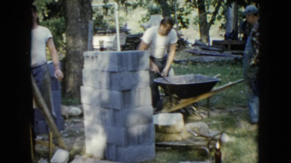 At the end of the clip, the concrete work continues beside stacked blocks, with a second adult partly cropped at the right edge.