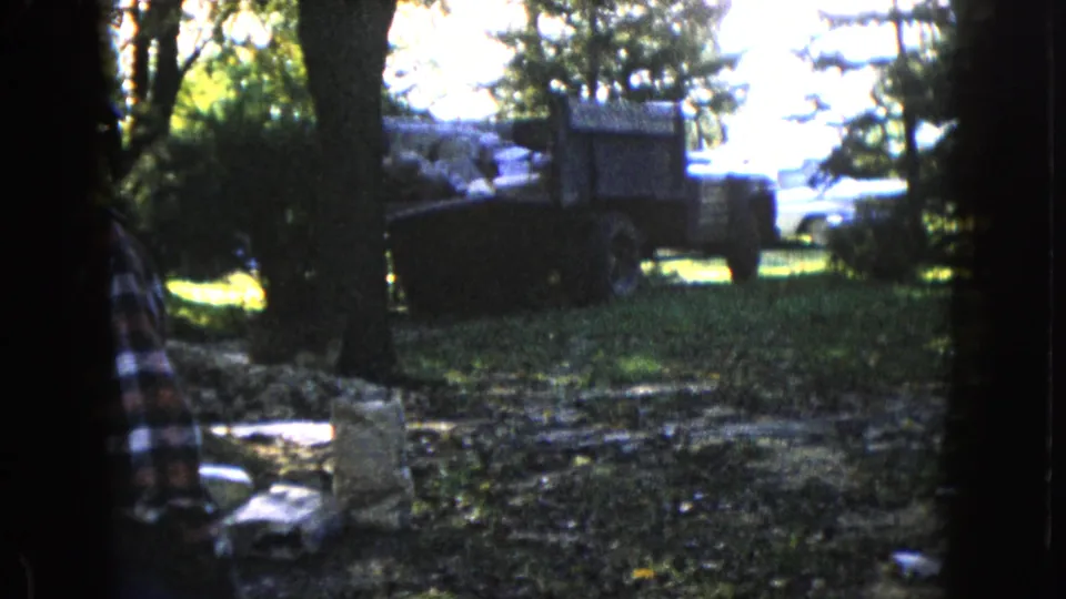 A loaded truck sits among trees in the Wauconda, Illinois work scene, with the plaid-shirted man partly cropped at left.
