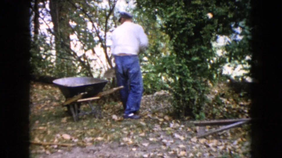 In Wauconda, Illinois, a man in a white shirt and blue jeans stands beside a wheelbarrow in a leafy wooded yard.