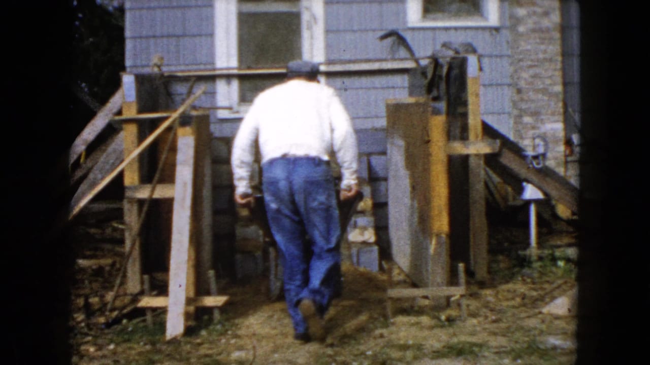 Man walks toward wood forms and stonework near the side of a house.