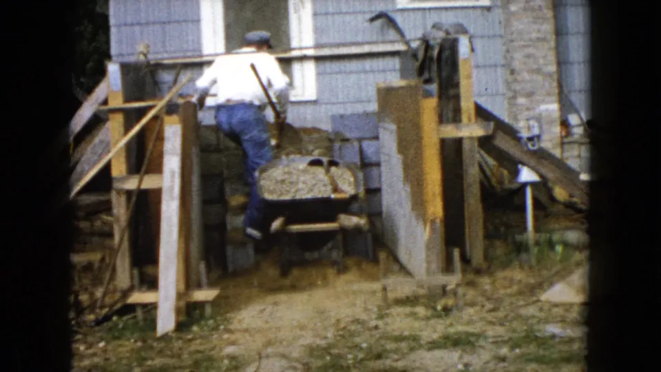 A man pushes a wheelbarrow filled with gravel through the residential work area in 1960 Wauconda, Illinois footage.