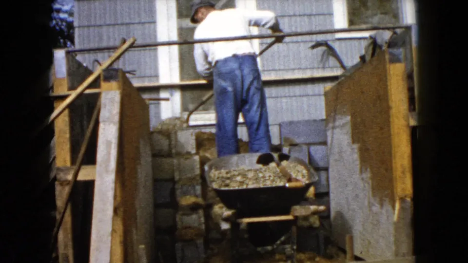 At the Wauconda, Illinois site, the man turns toward the foundation area with a shovel near the wheelbarrow of gravel.