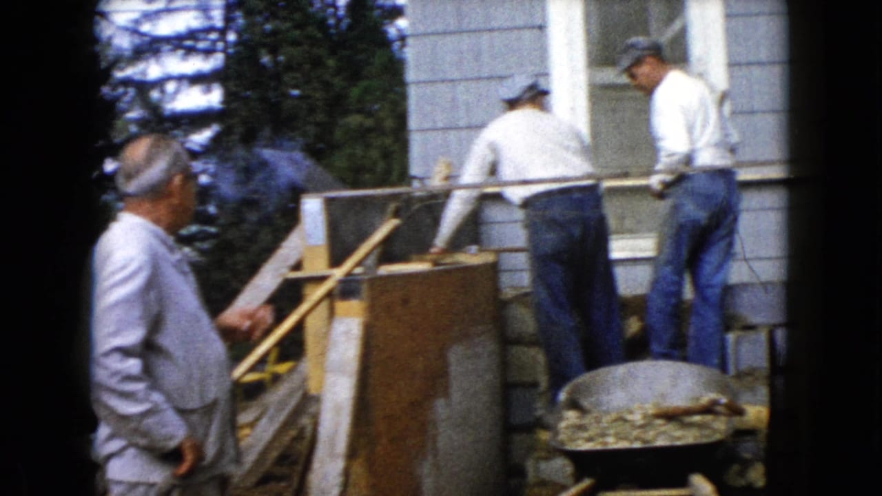In Wauconda, Illinois in 1960, men work beside a house on a small brick or masonry structure with a wheelbarrow in front.