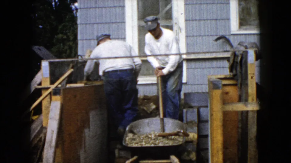 At the end of the clip, the men remain beside the Wauconda house with a wheelbarrow, tools, and masonry materials visible.