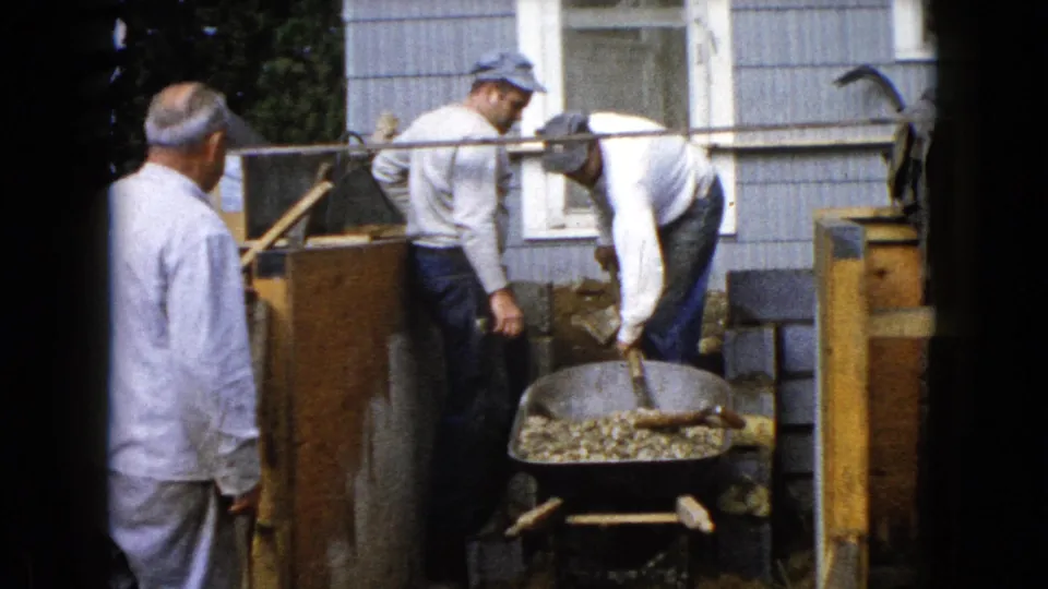 Three adult men work around a gravel-filled wheelbarrow outside a Wauconda house in 1960 home-movie footage.