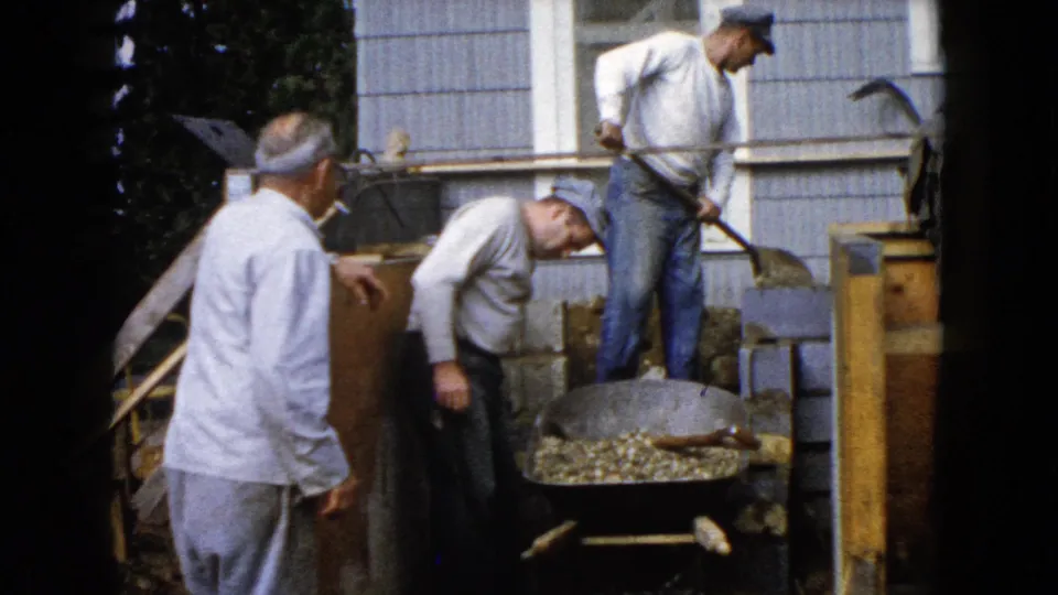At the end of the clip, one man stands on boards while another bends near the gravel-filled wheelbarrow outside the Wauconda house.
