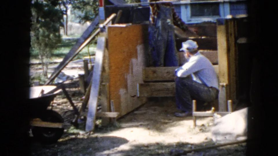 A man in a cap sits near wooden formwork for a stair project outside a house in Wauconda, Illinois, in 1960.