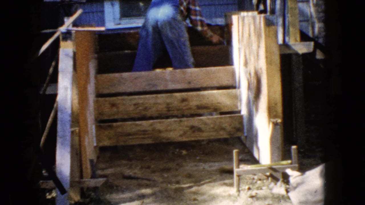 The 1960 Wauconda frame shows a man partially visible above a rough wooden frame, with house siding and a window behind him.