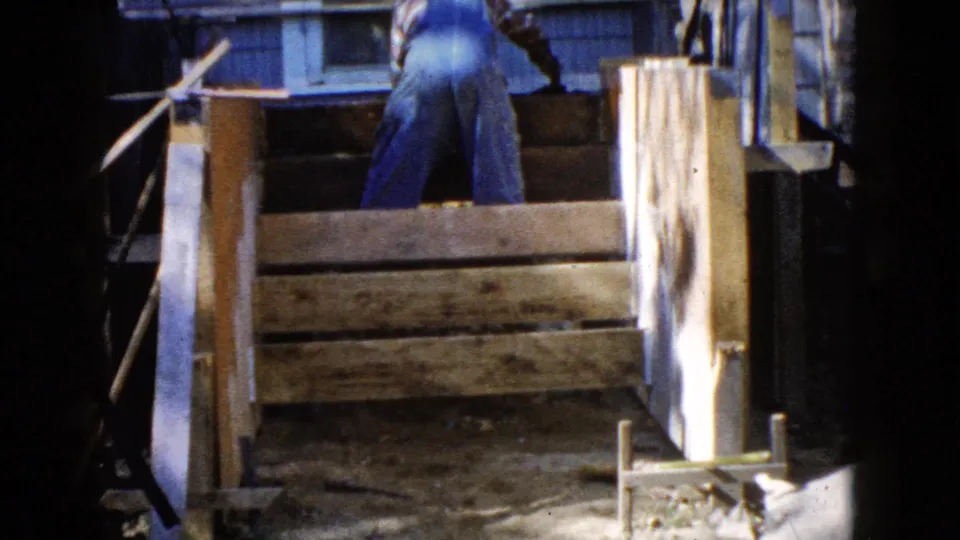 The final Wauconda, Illinois frame shows a man in blue overalls behind a low wooden enclosure or frame beside house siding.